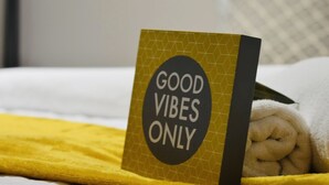 En seng med et gult tæppe og et skilt, der står 'GOOD VIBES ONLY'.