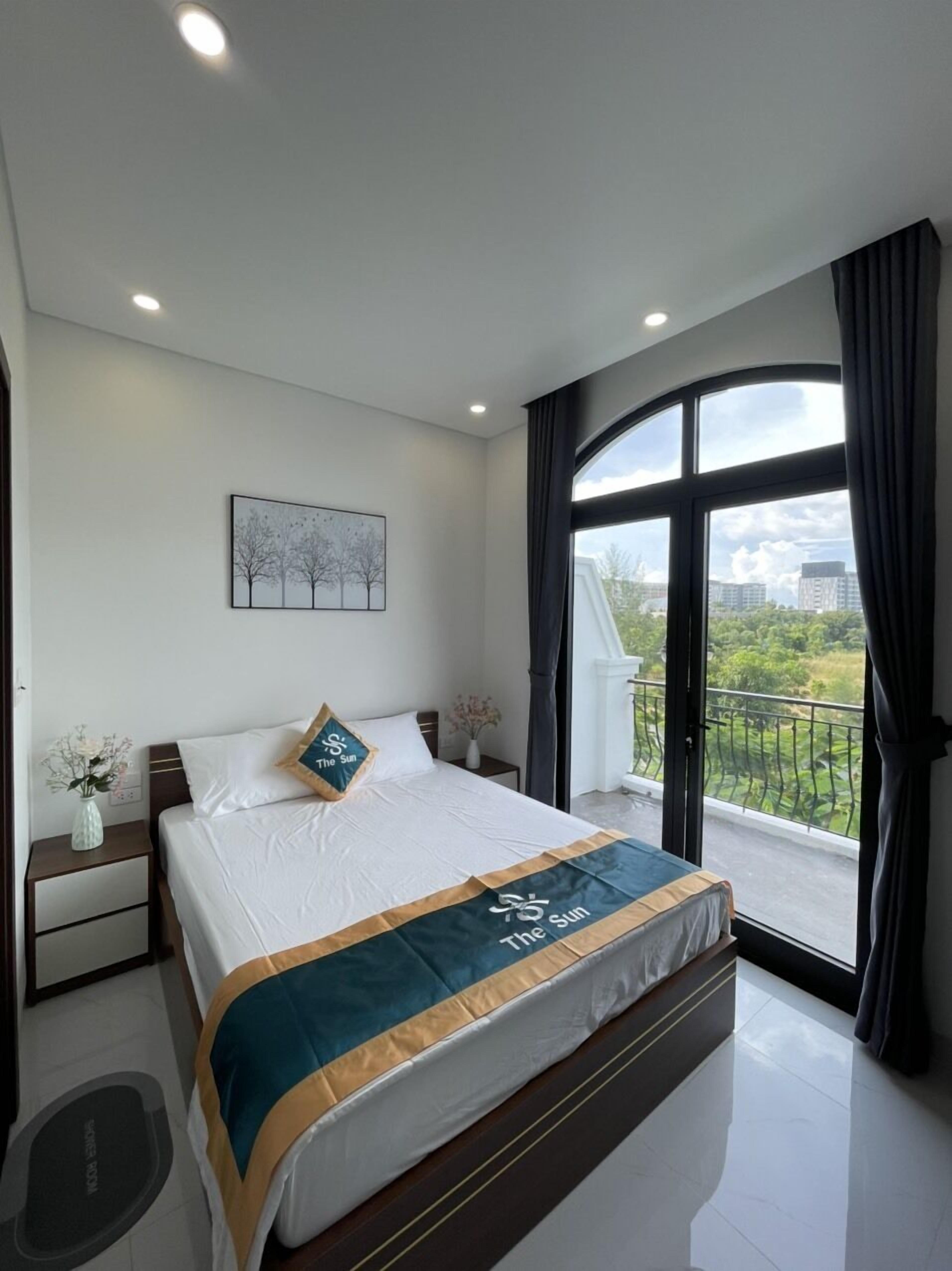 Une chambre moderne avec un grand lit, une table de chevet, un vase de fleurs, un tableau au mur et un balcon avec vue.