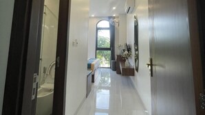 A hallway with a bathroom on the left, a bed with a view to the outside on the right, and a door at the end. - Homestay the Sun Grand World (Phu Quoc)