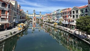 A canal with buildings on either side, a clear sky, and a bridge in the distance. - Homestay the Sun Grand World (Phu Quoc)