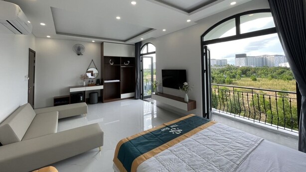 A modern hotel room with a large bed, a sofa, a TV, and a balcony with a city view. - Homestay the Sun Grand World (Phu Quoc)