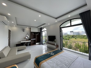 A modern hotel room with a large bed, a sofa, a TV, and a balcony with a city view. - Homestay the Sun Grand World (Phu Quoc)