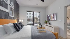 A modern bedroom with a large bed, a ceiling fan, a TV, and a view of the outside.