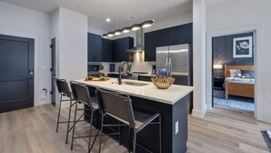 A modern kitchen with a central island, bar stools, and a large refrigerator.