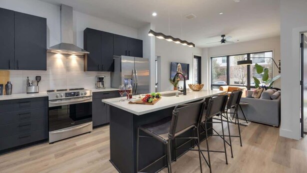 A modern kitchen with dark cabinetry, stainless steel appliances, and a central island with bar stools.