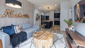 A modern living room with a light blue sofa, a round wooden coffee table, and a kitchen in the background.