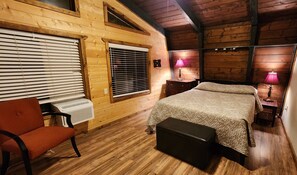 Une chambre confortable, aménagée dans un chalet en bois, avec un lit, une chaise, un radiateur et deux lampes.