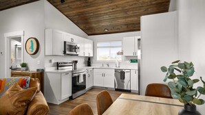 A modern kitchen with white cabinets, stainless steel appliances, and a wooden ceiling. - The Kabins - Camp Misery (Columbia Falls)