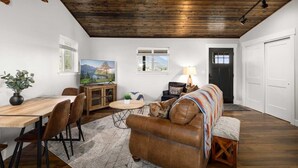 A spacious living room with a wooden ceiling, a sofa, a dining table, and a television. - The Kabins - Camp Misery (Columbia Falls)