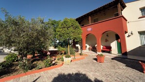 A courtyard with a red building, a tree, and potted plants. - Room-camagna Country House Scopello Room (Partanna)