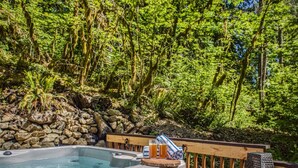 A hot tub surrounded by a wooden deck and lush greenery.