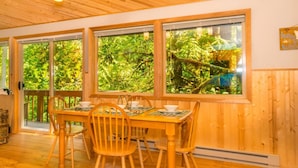 A wooden-paneled room with a large table and chairs, large windows with a view of greenery, and a wooden ceiling.