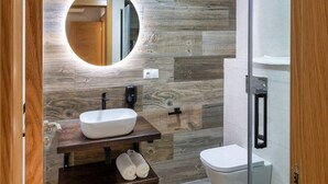 Une salle de bain moderne avec un meuble-lavabo en bois, un miroir rond, un lavabo blanc et des toilettes.