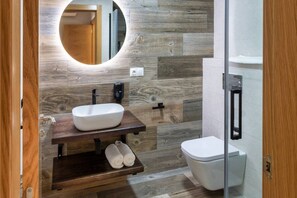 A modern bathroom with a wooden vanity, a round mirror, a white sink, and a toilet.