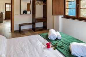A hotel room with a bed, a green bedspread, two rolled towels, a red rose, and a wooden bench.