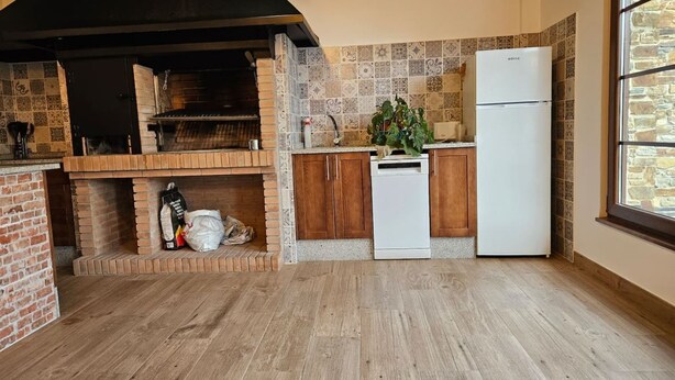 Een keuken met een bakoven, houten kasten, een witte koelkast en een raam met uitzicht op een stenen muur.