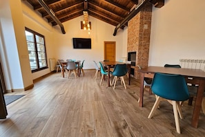 A dining area with a brick fireplace, wooden ceiling beams, and a TV mounted on the wall. - 28B01 Aptos Lola Penarronda -Fontias (Castropol)