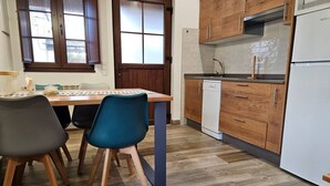 Een kleine keuken met houten kastjes, een vaatwasser en een eethoek met twee stoelen.