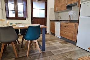 A compact kitchen with wooden cabinets, a dishwasher, and a dining area with two chairs. - 28B01 Aptos Lola Penarronda -Fontias (Castropol)
