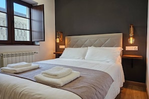 A bedroom with a large bed, two bedside lamps, a window, and a radiator. - 28B01 Aptos Lola Penarronda -Fontias (Castropol)