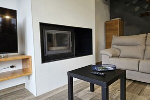 A modern living room with a flat-screen TV, a fireplace, a wooden cabinet, and a beige sofa. - 28B01 Aptos Lola Penarronda -Fontias (Castropol)