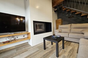 A modern living room with a flat-screen TV, a fireplace, a sofa, and a staircase.