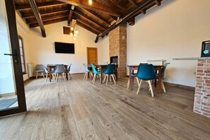 A dining area with wooden flooring, a brick fireplace, and teal chairs.