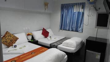 A hotel room with two single beds, a small desk, a fan, a TV, and a window with curtains.