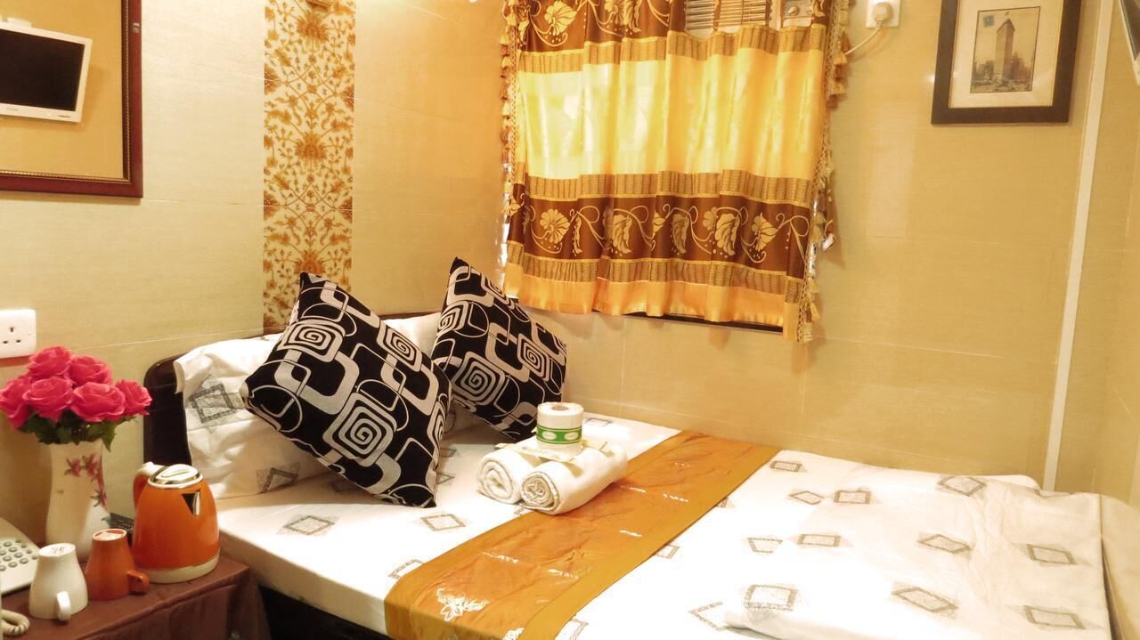 A neatly made bed with patterned pillows, a bedside table with a vase of flowers, a kettle, and a phone.