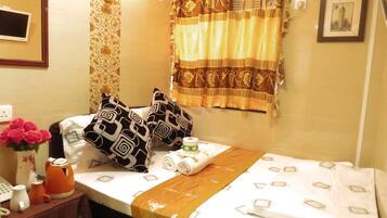 A neatly made bed with patterned pillows, a bedside table with a vase of flowers, a kettle, and a phone.