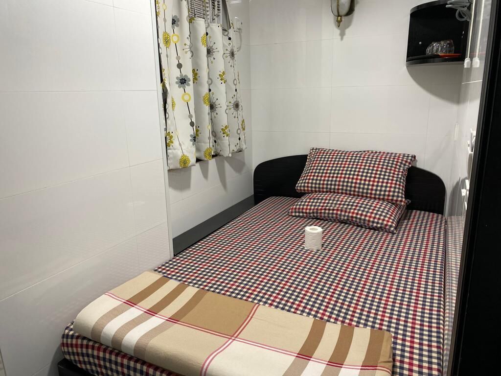 A small, neatly made bed with a checkered bedspread and matching pillow, a white toilet, and a shower curtain with a floral pattern.