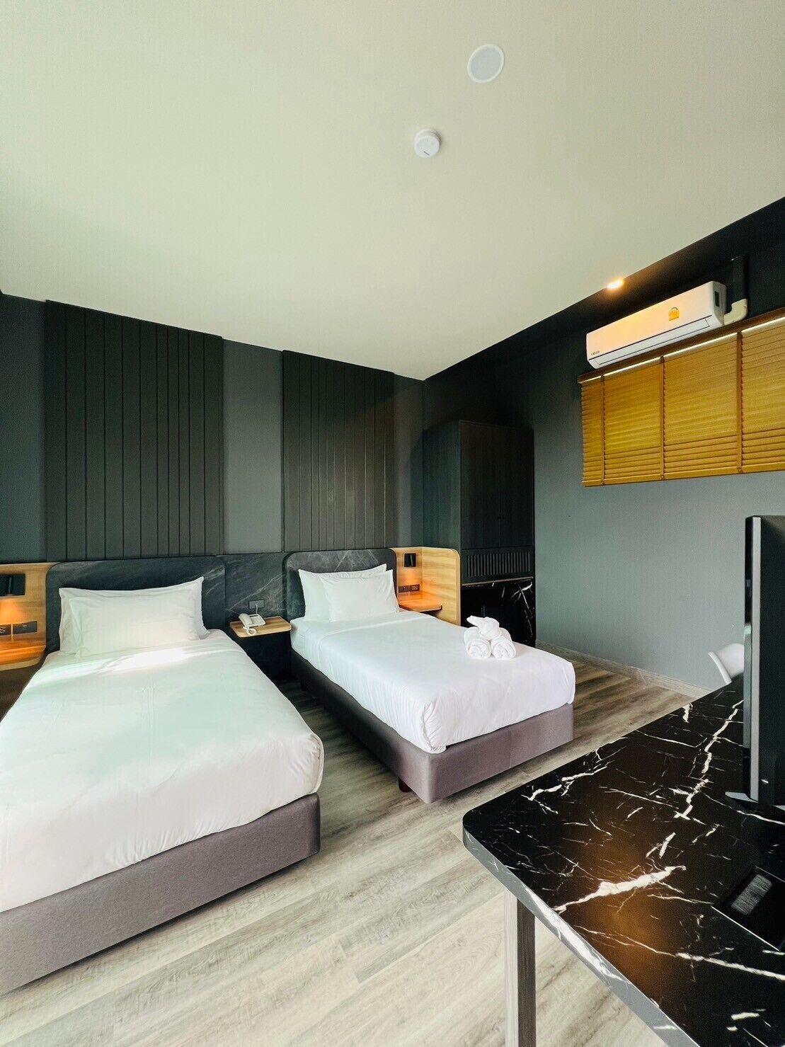 A modern hotel room with two beds, a marble-topped table, and an air conditioning unit.