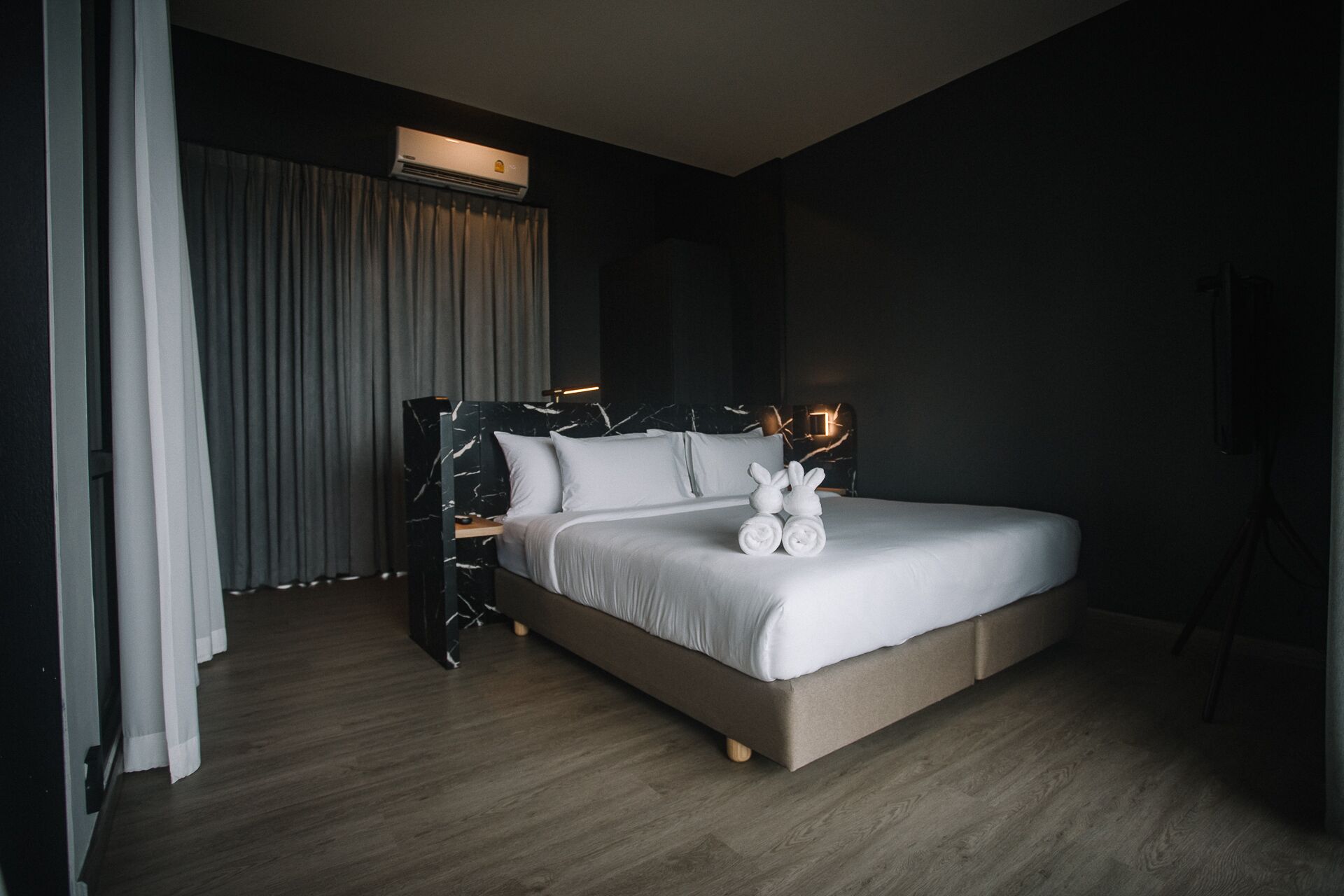 A modern hotel room with a large bed, a marble headboard, and a neatly made bed with rolled towels.
