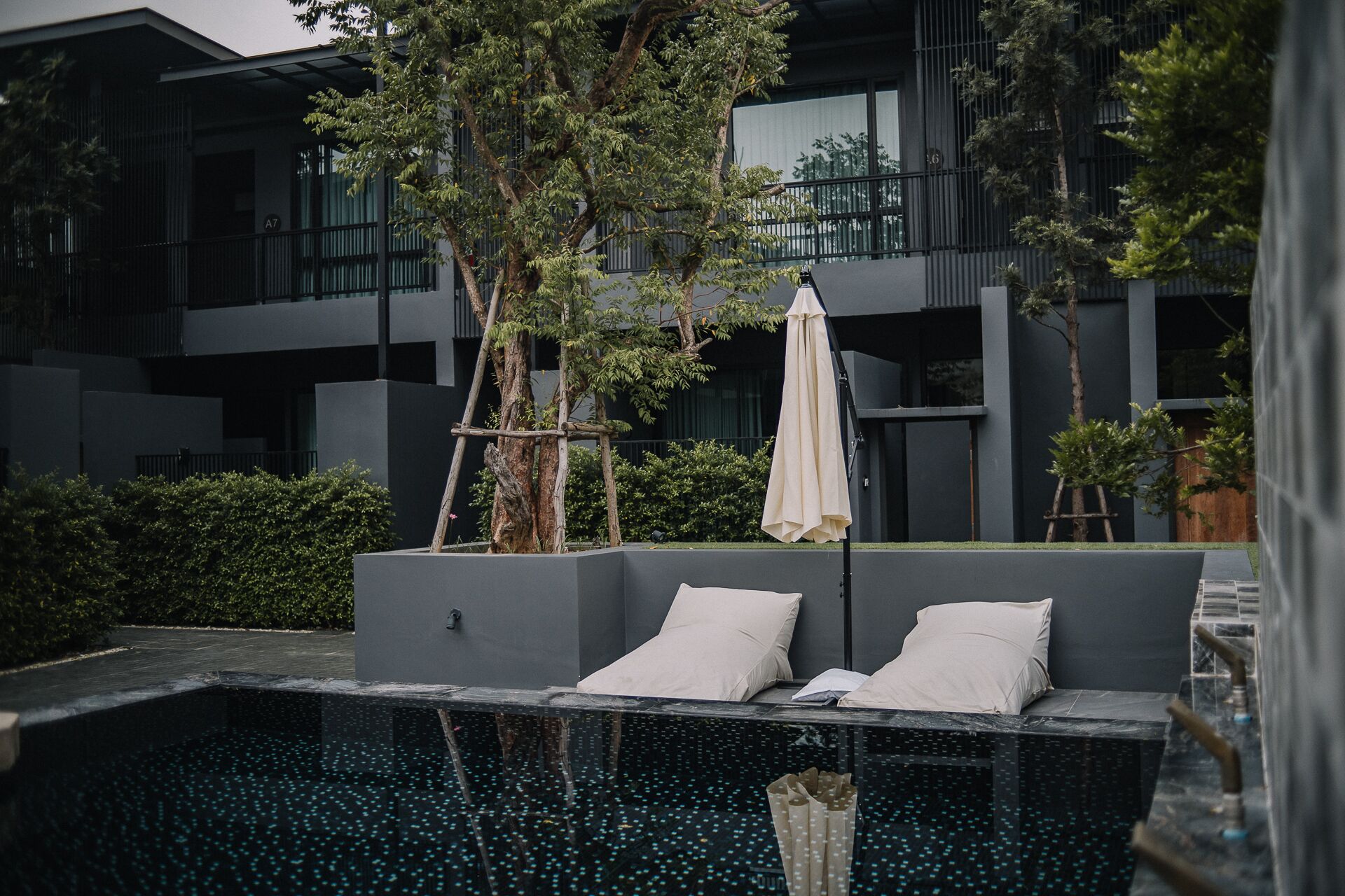 A modern outdoor pool area with a seating area, surrounded by greenery and a building with large windows.