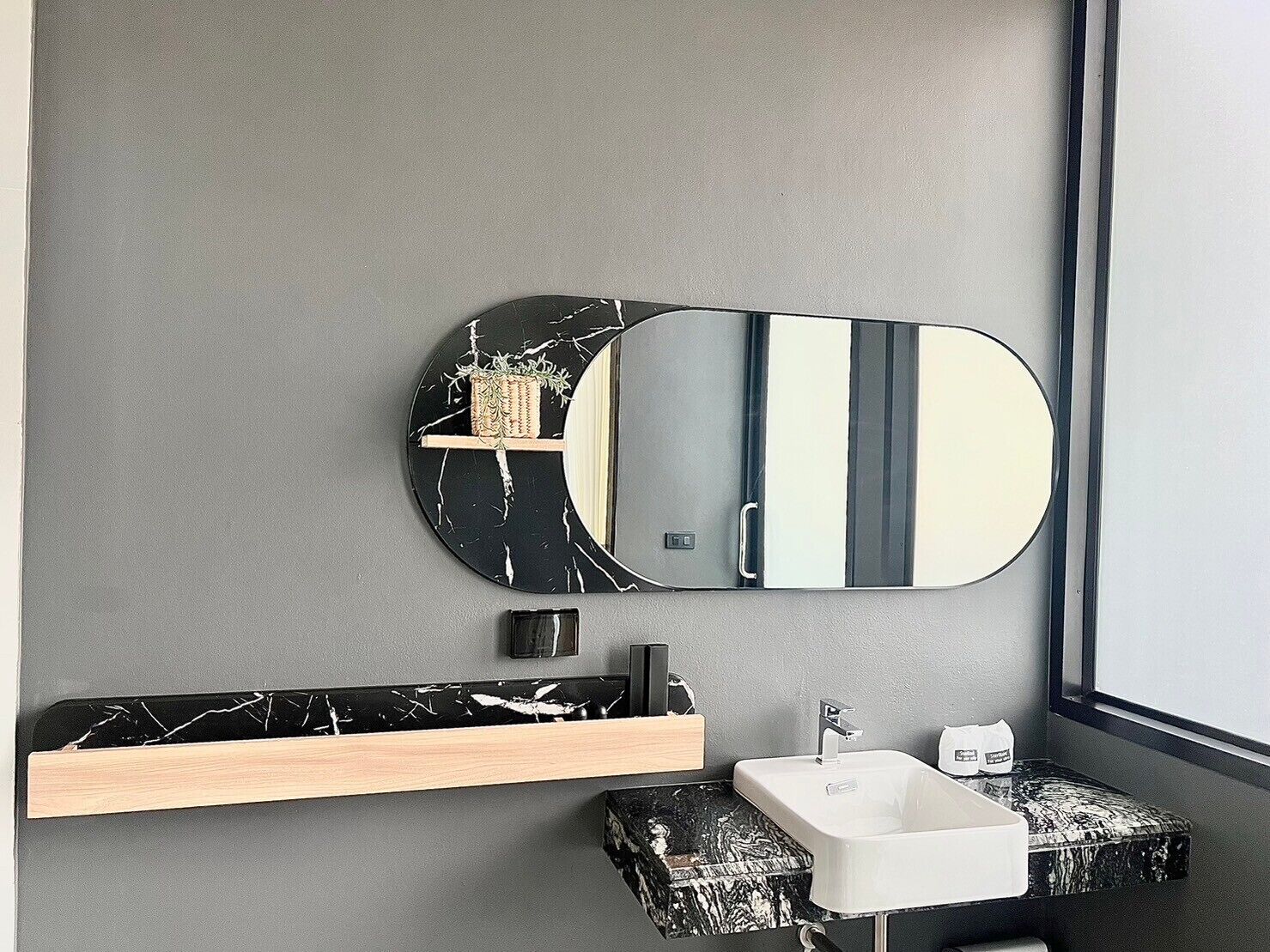 A modern bathroom with a marble vanity, a white sink, and a large mirror.