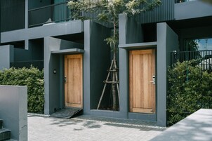A modern building with two wooden doors, a small wooden staircase, and a ladder leading to a balcony.