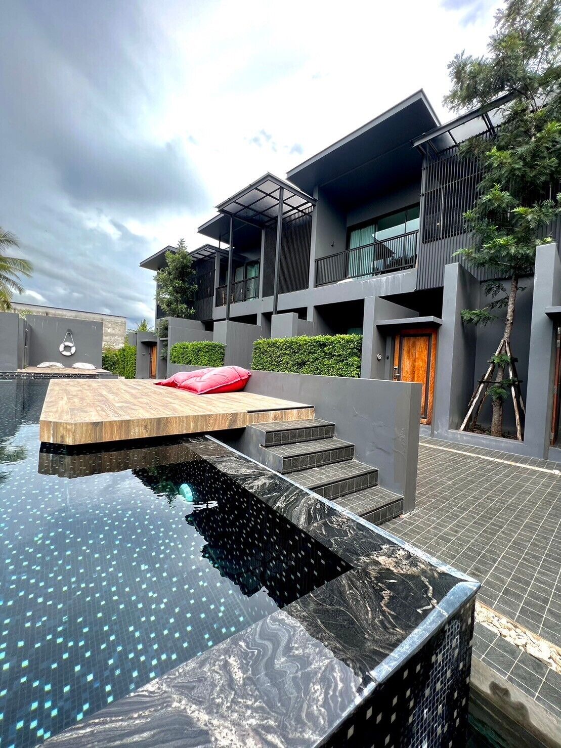A modern building with a rooftop pool, steps leading to a wooden deck, and a balcony.