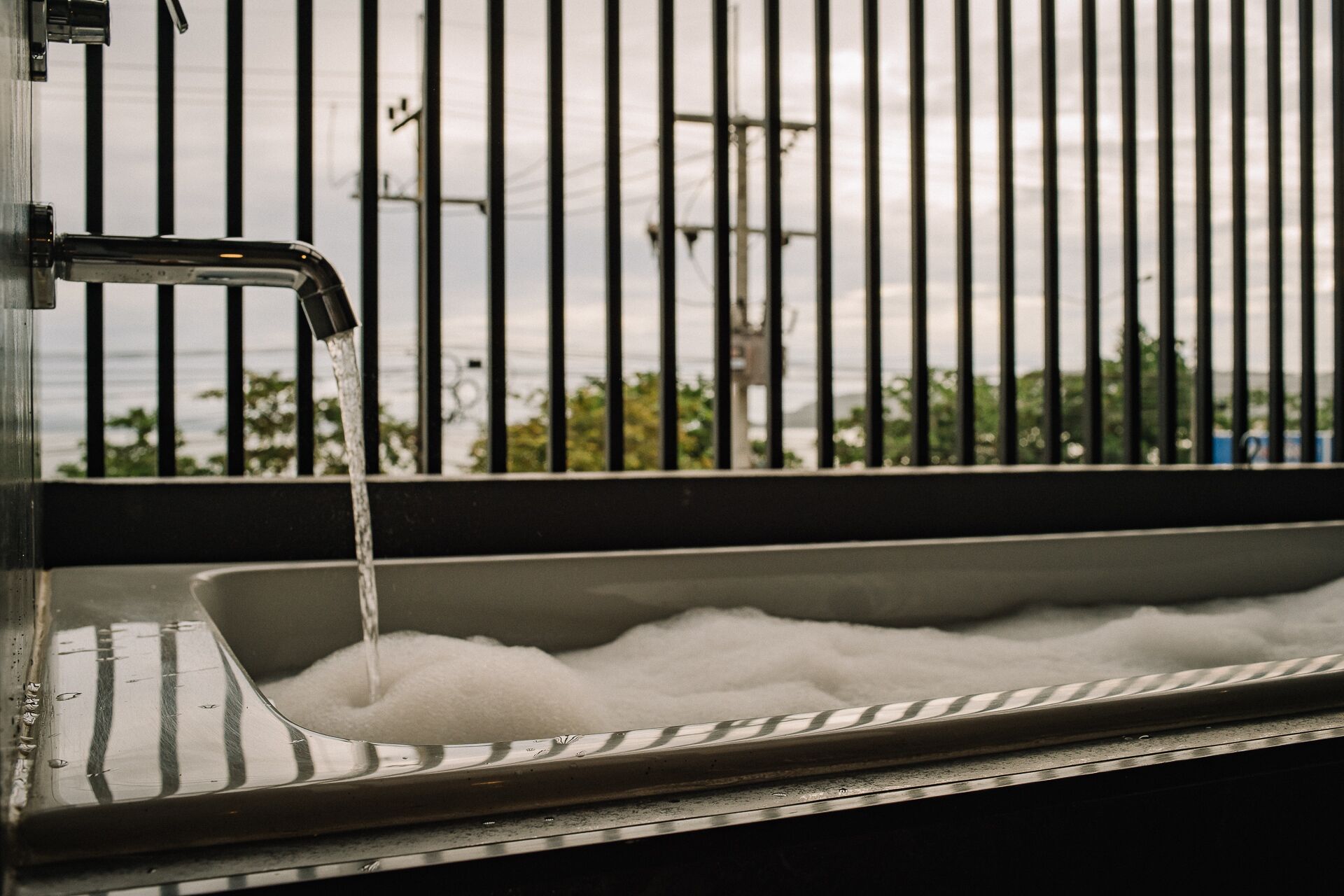 A window with vertical bars, a faucet, and a sink filled with water.