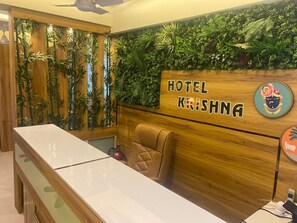 Una mesa de recepción con un cabecero de madera que dice "HOTEL KRISHNA" y una silla cómoda.