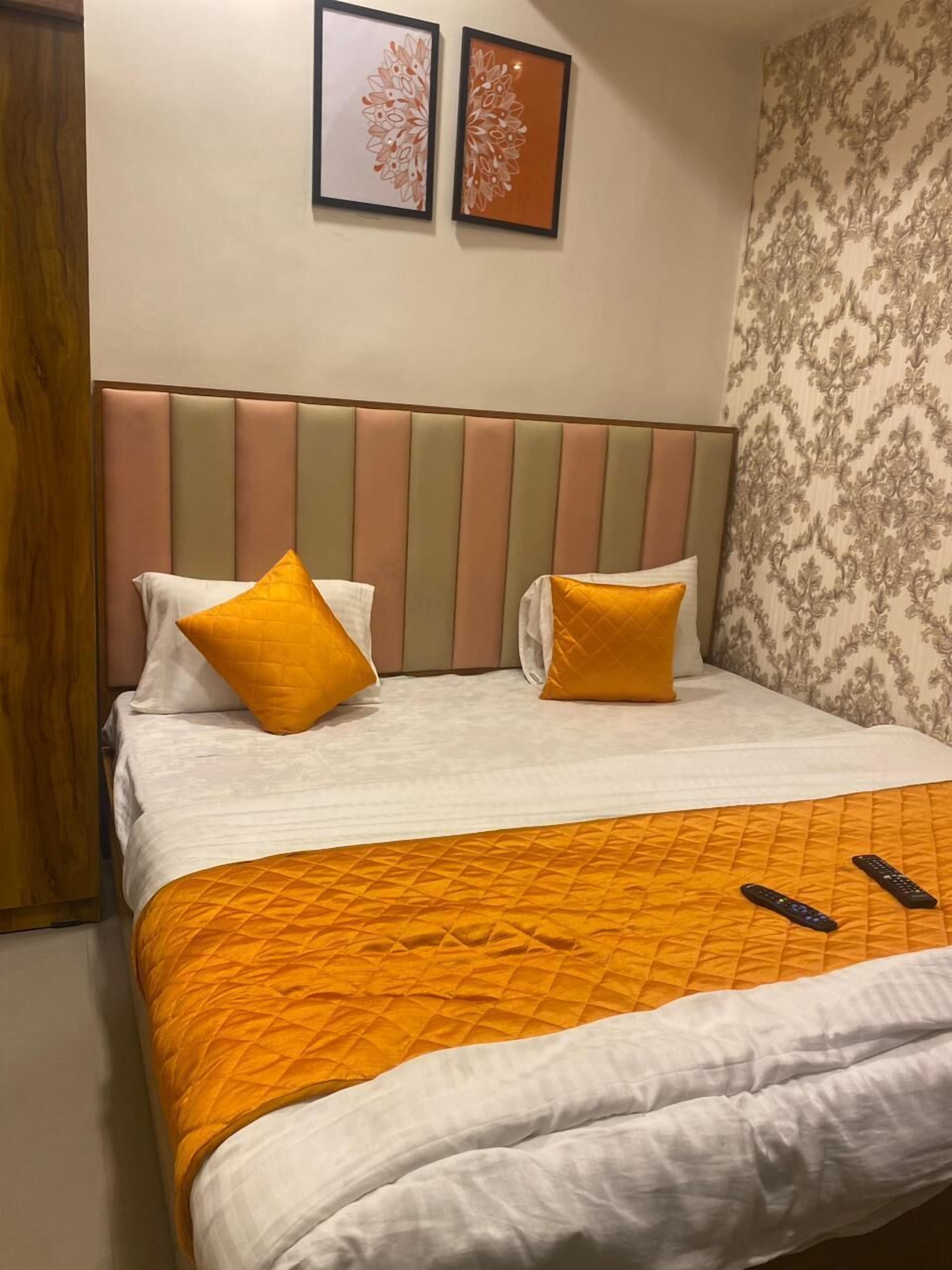 A neatly made bed with a striped headboard, two pillows, and a quilted orange blanket. Two remote controls are on the bed.
