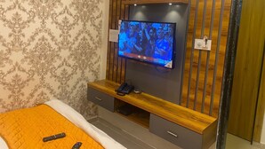 Ein Hotelzimmer mit an einer Holzvertäfelung montiertem Fernseher, einem Bett mit orangefarbener Steppdecke und einem Nachttisch aus Holz mit Telefon und Fernbedienungen.