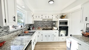 A modern kitchen with white cabinets, granite countertops, a black backsplash, and a built-in oven.