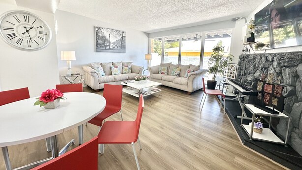 A modern living room with a sofa, dining table, and chairs, a clock, and a fireplace.