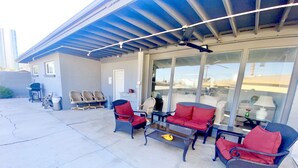 An outdoor patio with seating, a ceiling fan, and large windows offering a view of the cityscape.