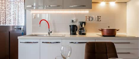 A modern kitchen with white cabinets, a red faucet, a coffee maker, and a pot on the counter.