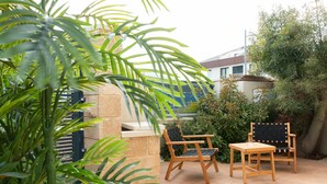 An outdoor patio area with a wooden table and two chairs, surrounded by greenery and a stone wall. - Huge & Lovely Unit 2BR 2BT By the beach (Rishon LeTsiyon)
