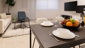 A modern living room with a dining area, featuring a sofa, a blue chair, a dining table with plates and glasses, and a fruit bowl. - Huge & Lovely Unit 2BR 2BT By the beach (Rishon LeTsiyon)
