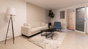 A modern living room with a white sofa, a coffee table, a floor lamp, and a potted plant. - Huge & Lovely Unit 2BR 2BT By the beach (Rishon LeTsiyon)