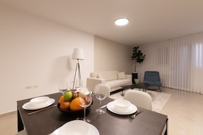 A dining area with a table set for four, a bowl of fruit, wine glasses, and a lamp. - Huge & Lovely Unit 2BR 2BT By the beach (Rishon LeTsiyon)
