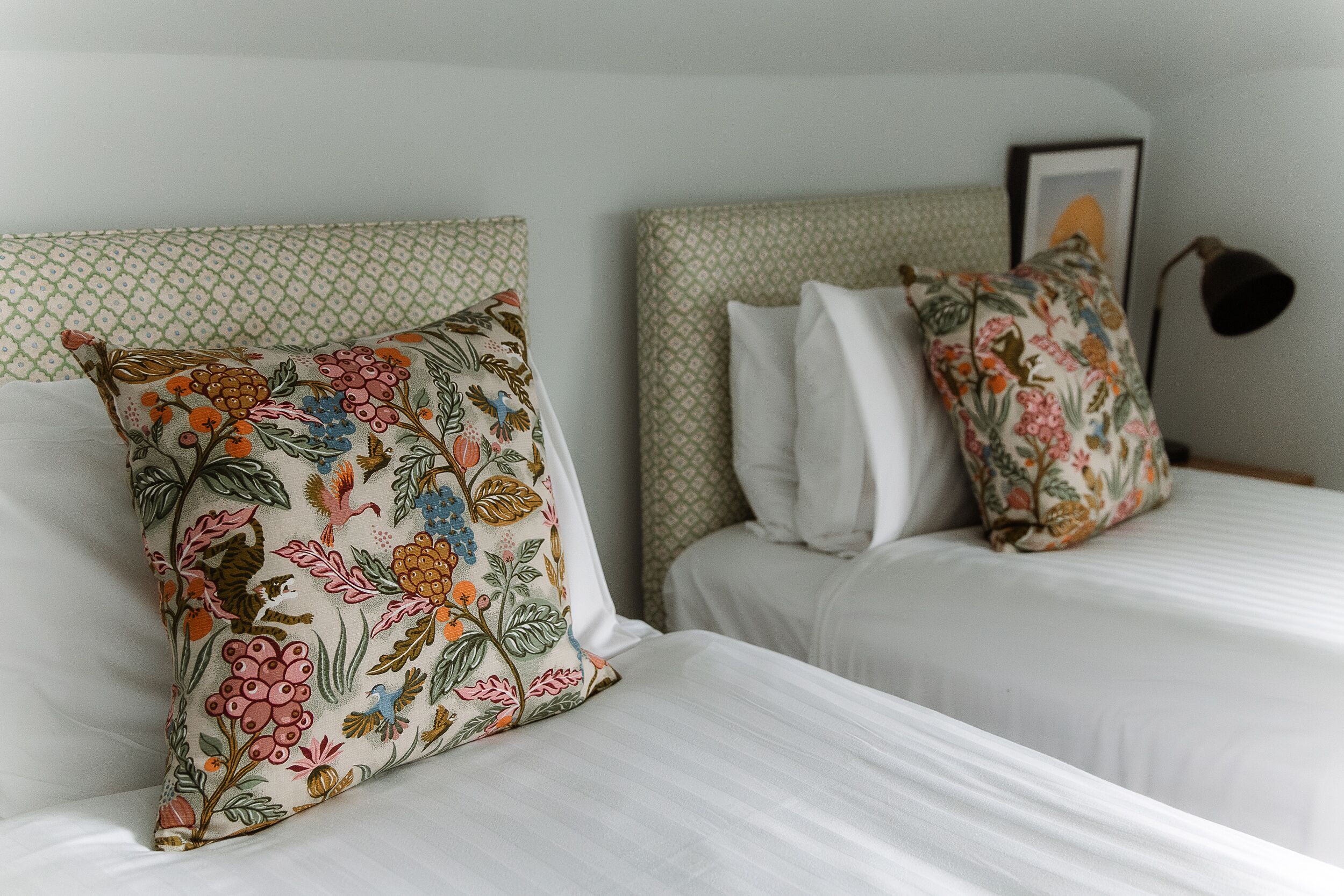 Two beds with white linens and floral-patterned pillows.